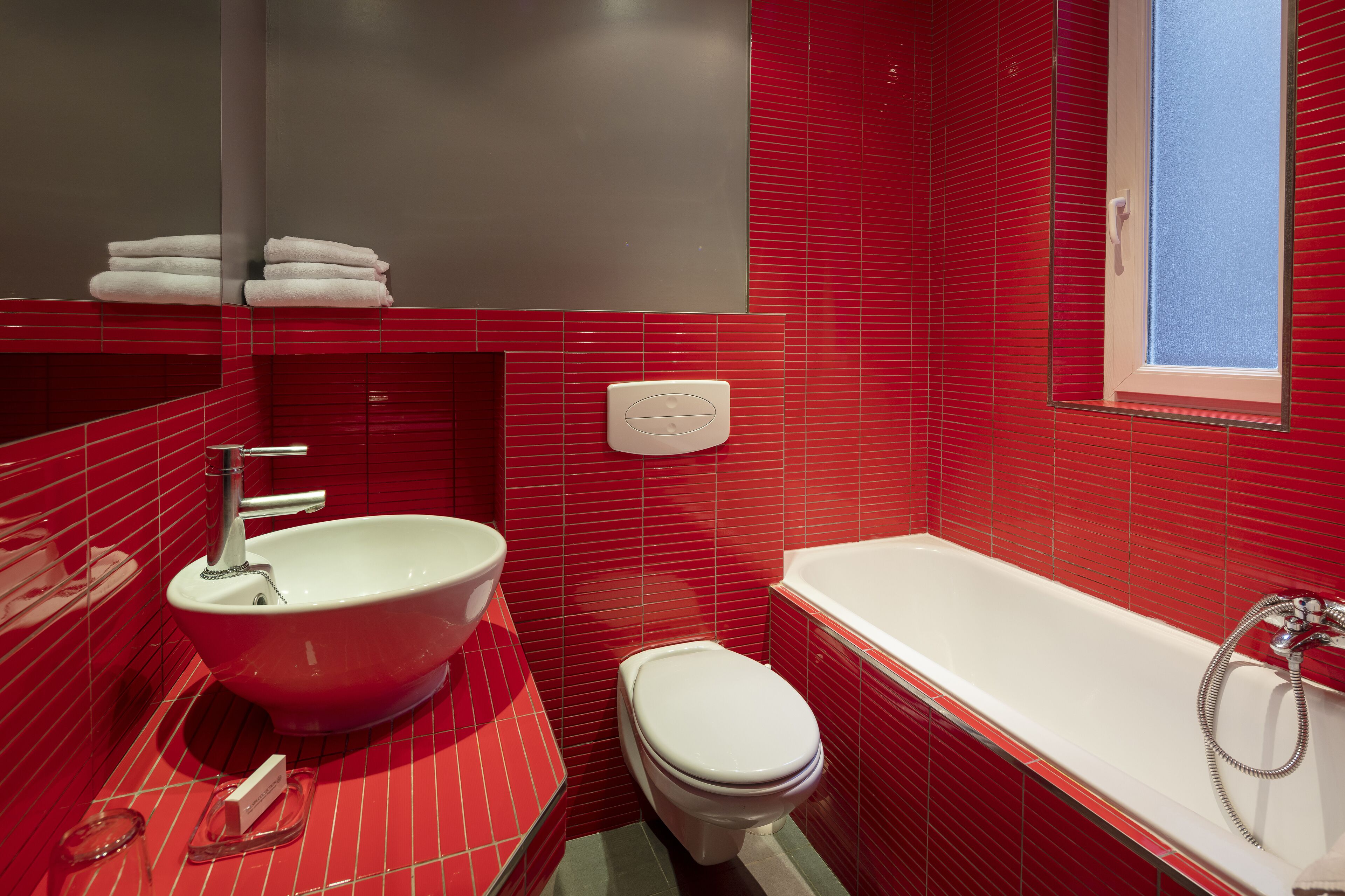 Een badkamer met een rode betegelde wand, een witte wastafel, toilet en een bad.