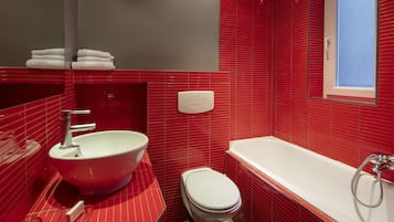 Een badkamer met een rode betegelde wand, een witte wastafel, toilet en een bad.