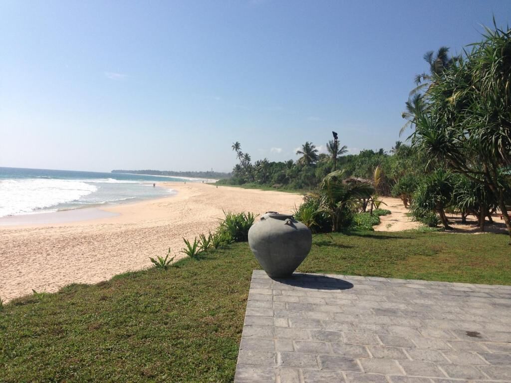 Vista de playa con una gran escultura de piedra al frente, palmeras y cielo despejado.