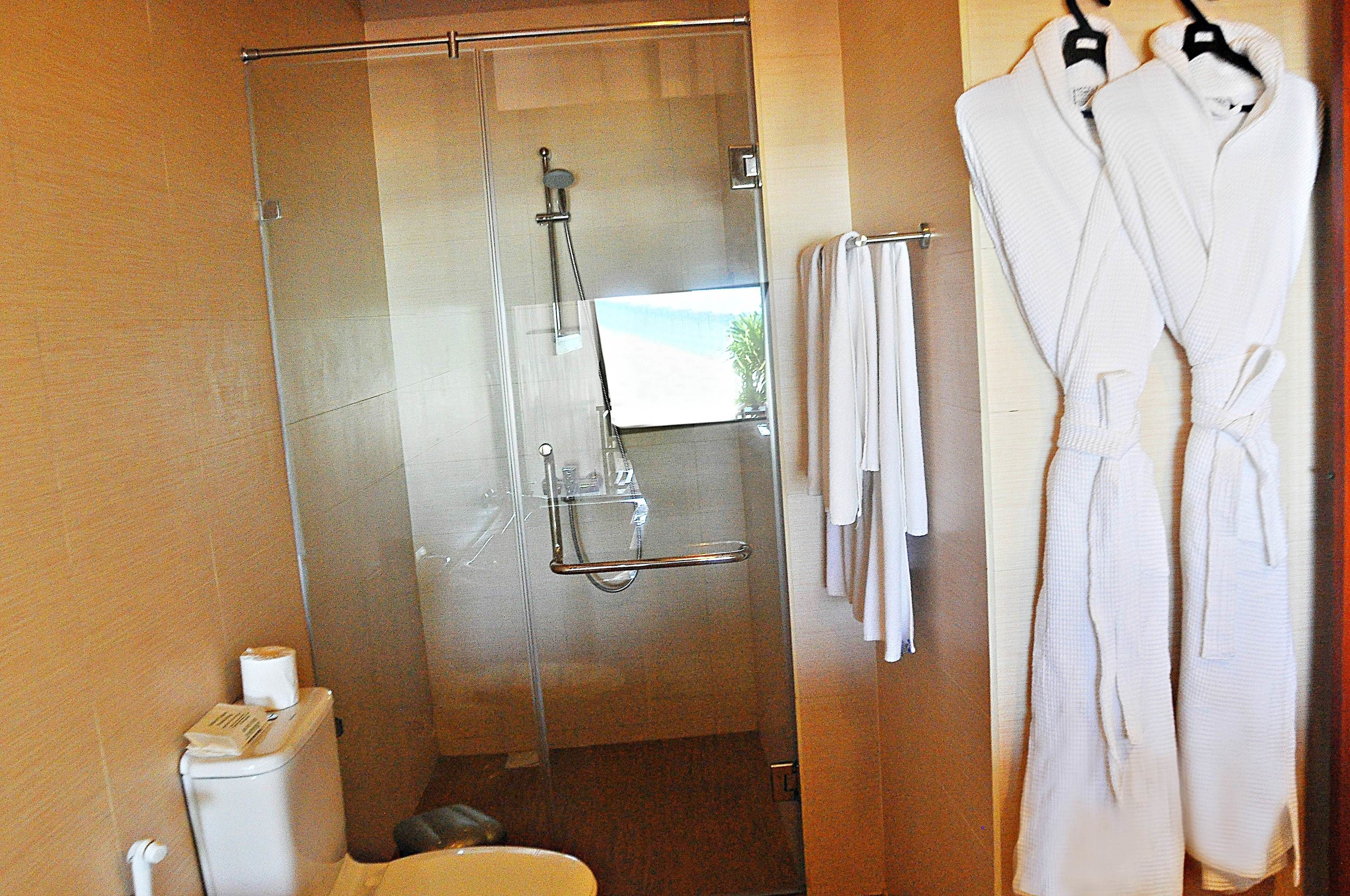 A bathroom with a glass-enclosed shower, a toilet, and a towel rack with towels.