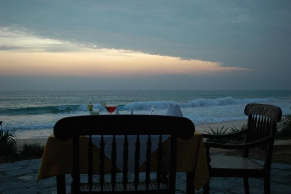 A beach view with a chair and a table, a drink on the table, and a sunset in the background.