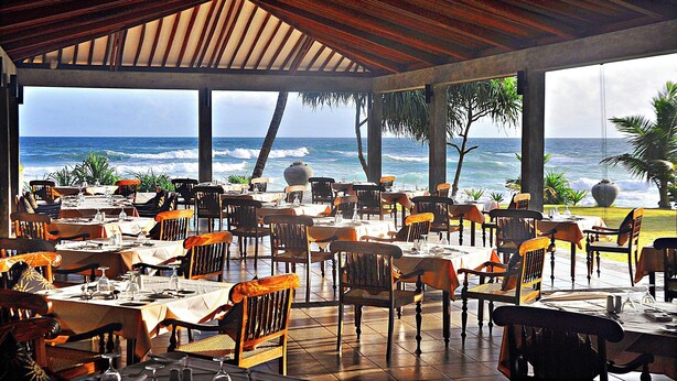 Restaurante al aire libre con mesas y sillas, con vista al océano.