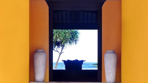 Una puerta que da a vista del océano, con una palmera y un jarrón grande a cada lado.