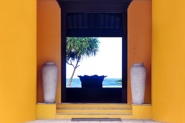 A doorway leading to a view of the ocean with a palm tree and a large vase on either side. - The Beach Cabanas (Koggala)