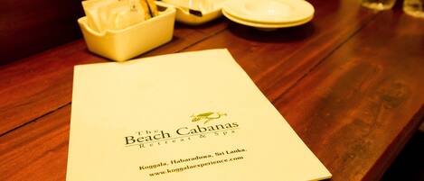 A menu on a wooden table with a bowl of bread and a plate.