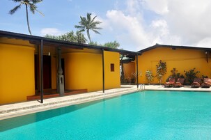 Un área de piscina con edificios amarillos, palmeras y sillones de descanso.