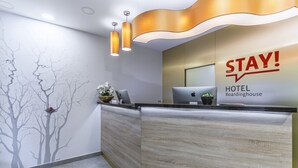 Una recepción de hotel de diseño moderno, con un letrero que dice 'STAY!', una computadora portátil y un florero con flores.