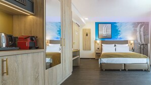 Habitación de hotel con dos camas, un minibar, un escritorio con cafetera y un mural en la pared.