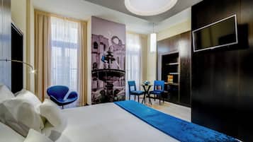 A hotel room with a large bed, a desk with two chairs, a flat-screen TV mounted on the wall, and a decorative fountain image on the wall.