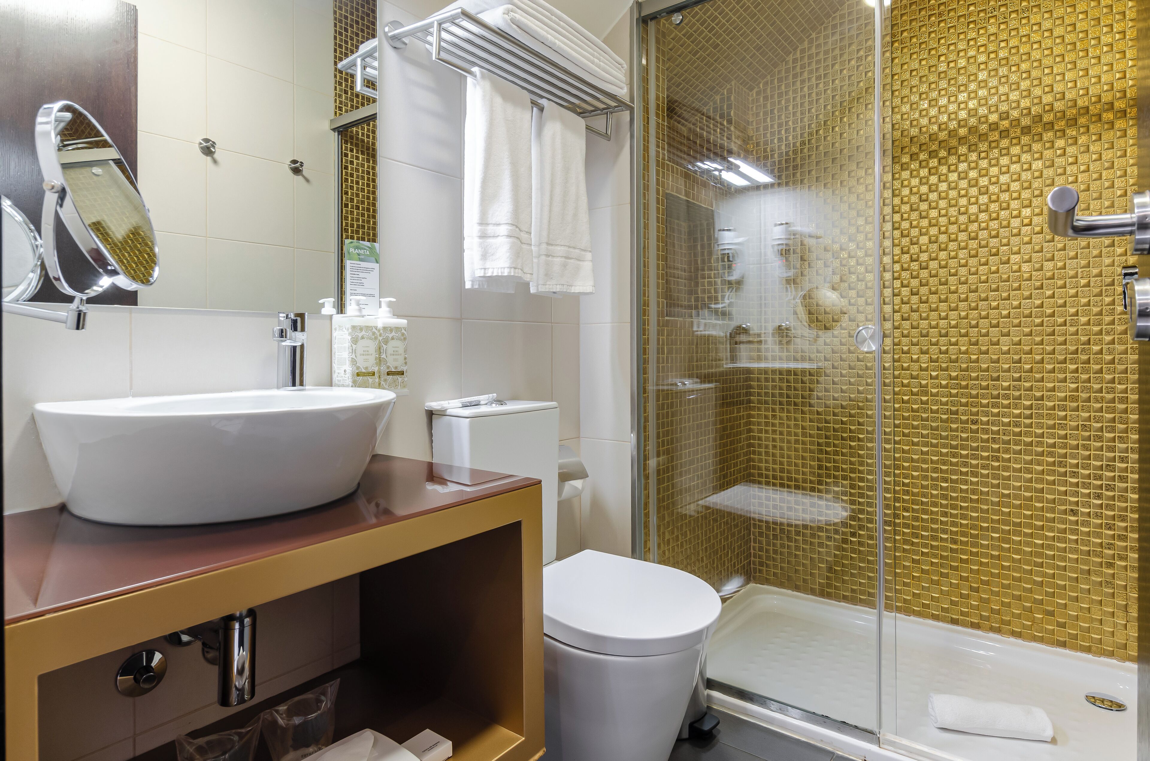 A bathroom with a large white sink, a toilet, a glass shower enclosure, and a mirror.