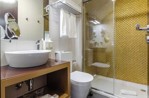 A bathroom with a large white sink, a toilet, a glass shower enclosure, and a mirror.