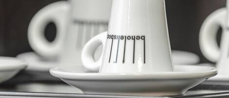 A close-up of a white ceramic cup with a handle and a saucer, featuring a design with vertical lines and text.