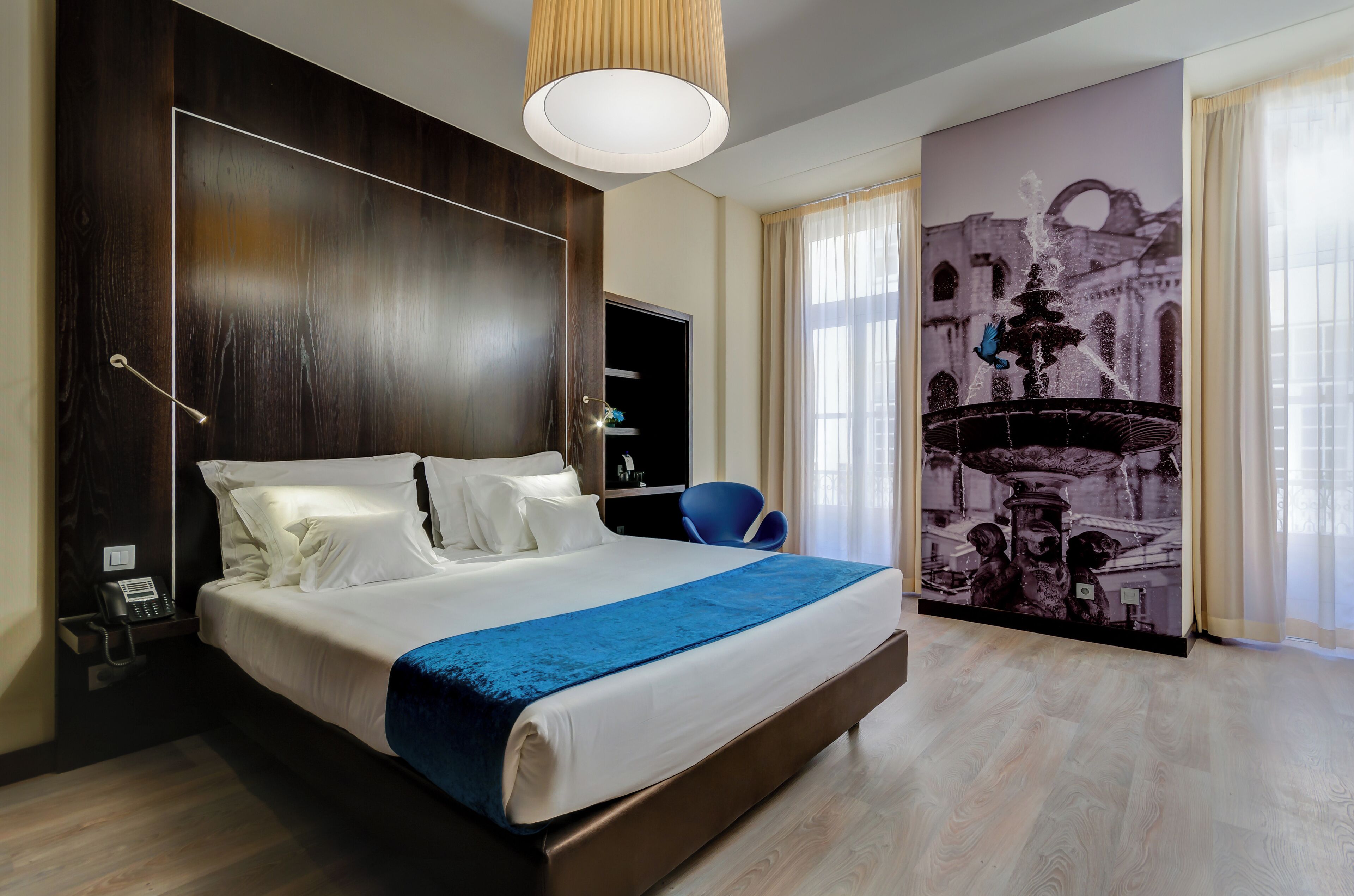 A hotel room with a large bed, a desk with a telephone, and a wall-mounted TV.