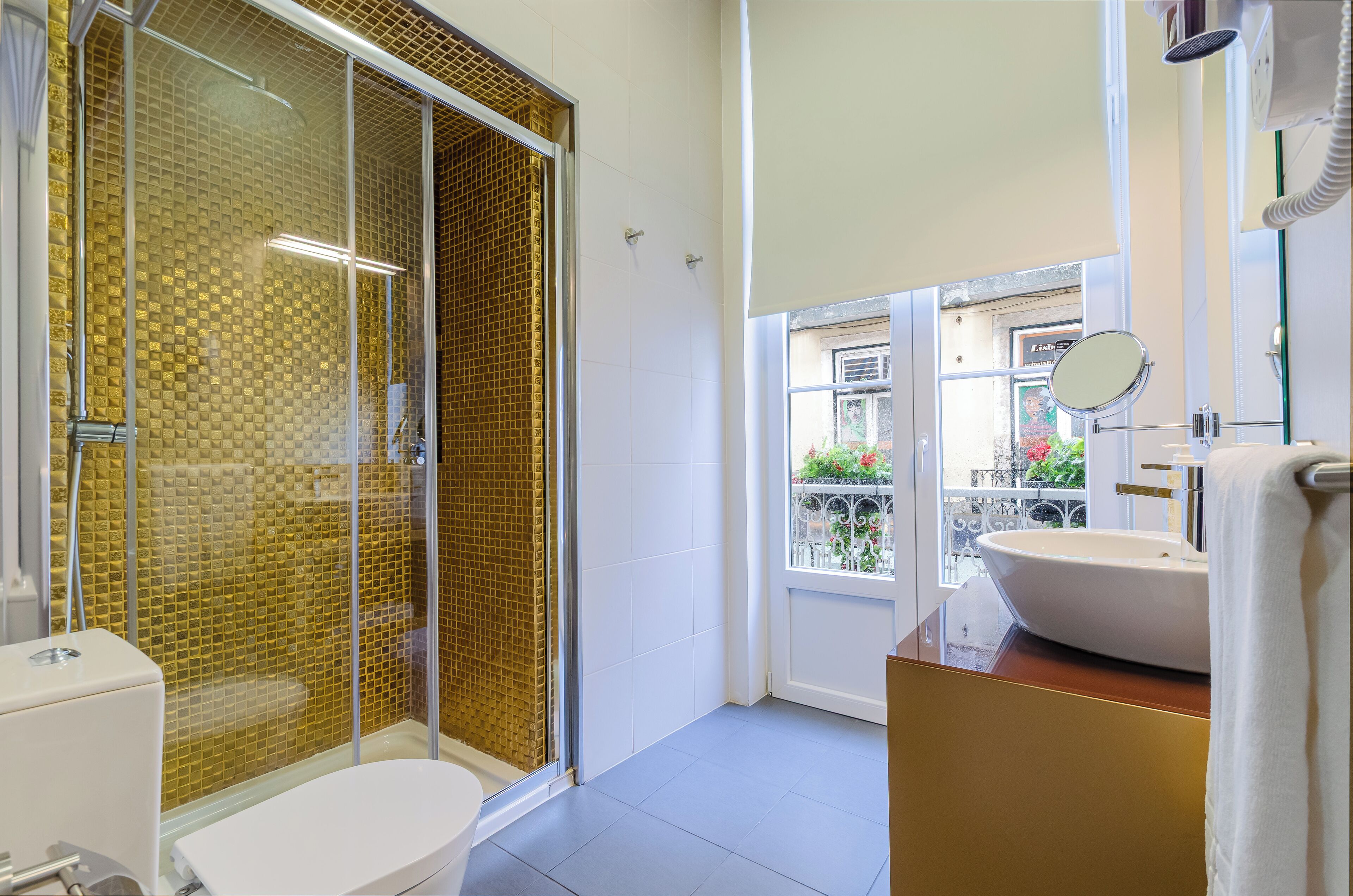 A modern bathroom with a glass-enclosed shower, a white sink, and a view of the outside balcony.