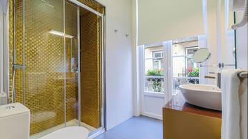 A modern bathroom with a glass-enclosed shower, a white sink, and a view of the outside balcony.