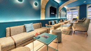 A modern lounge area with sofas, armchairs, and a coffee table, featuring a stone wall and a flat-screen TV. - Behotelisboa (Lisbon)