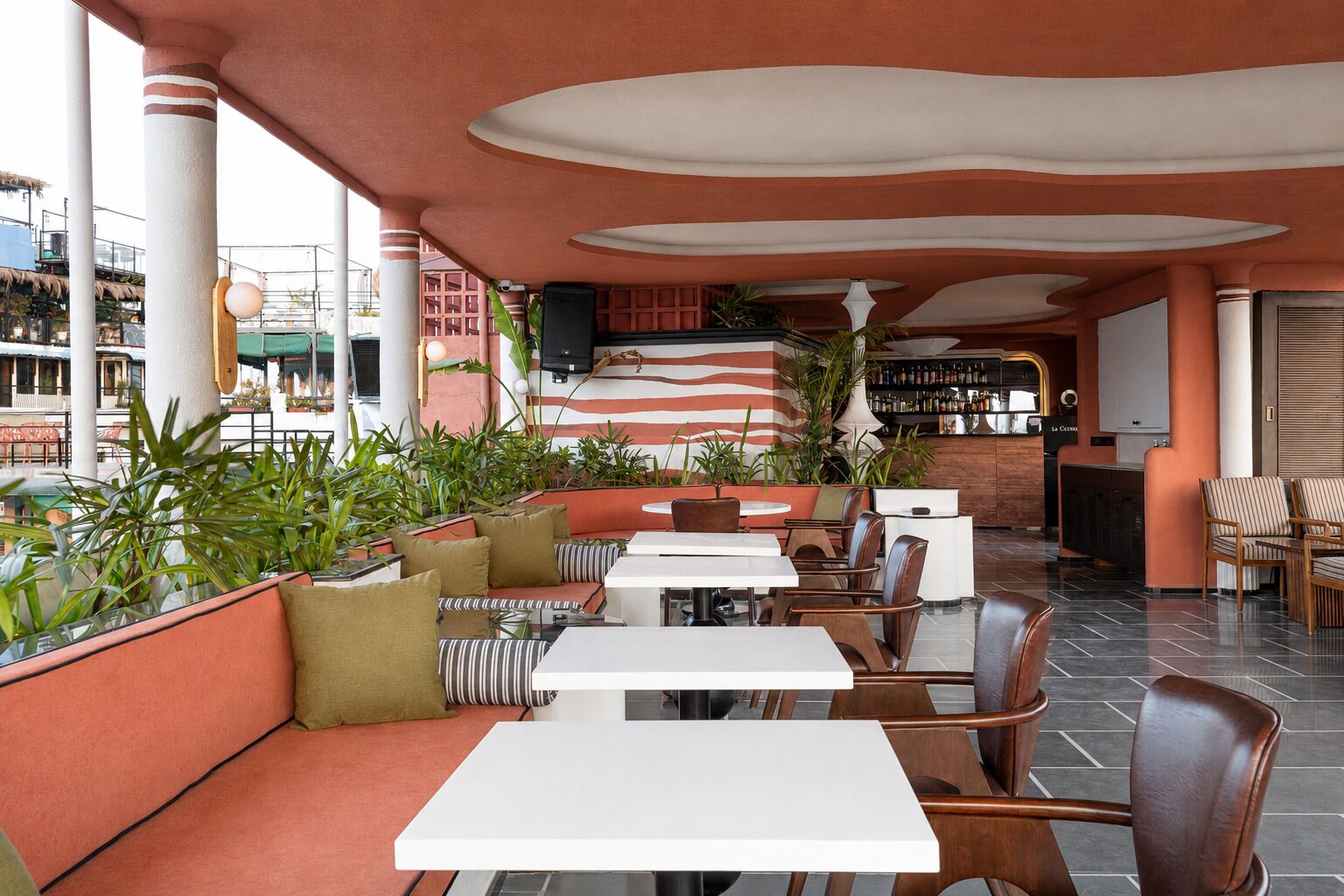 An outdoor seating area with tables and chairs, surrounded by plants and a bar area.