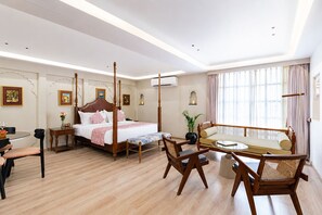 A hotel room with a four-poster bed, a sofa, a dining table, and a chair.