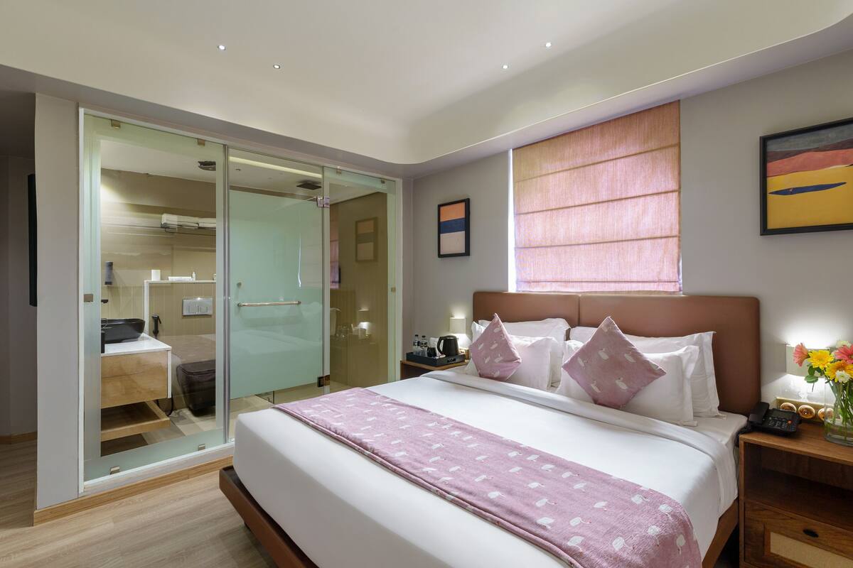 A hotel room with a bed, bedside table, and a glass-enclosed bathroom.