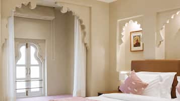 A bedroom with a bed, a nightstand, a window with curtains, and a door with decorative moldings.