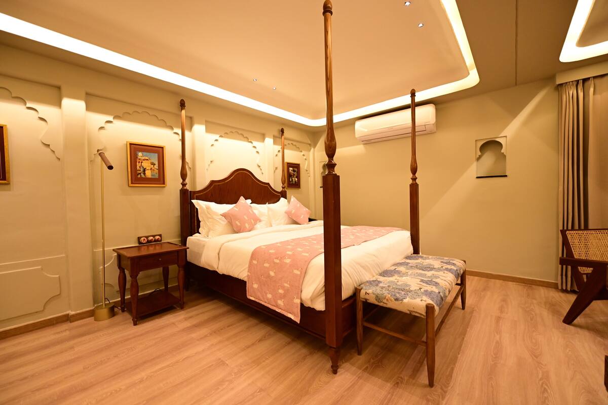 A four-poster bed with a wooden frame, a bedside table, a bench, and a wall-mounted air conditioning unit.