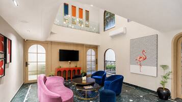 Un vestíbulo moderno con piso de mármol, un sillón rosa, sillones azules, una mesa redonda y un televisor montado en la pared.