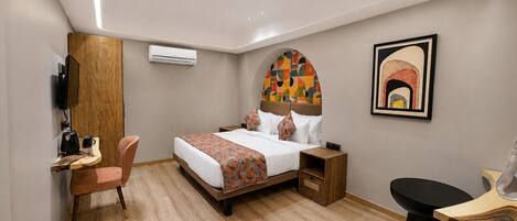 Habitación de hotel con cama, escritorio, silla, televisor y aire acondicionado.