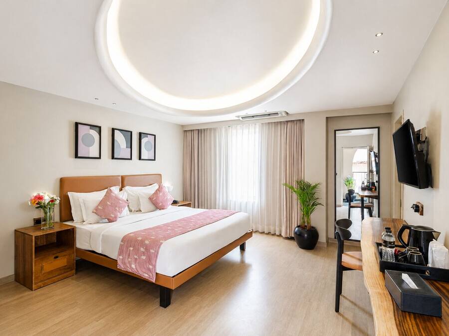 Una habitación de hotel moderna con cama, mesita de noche, planta en maceta y un escritorio con silla.