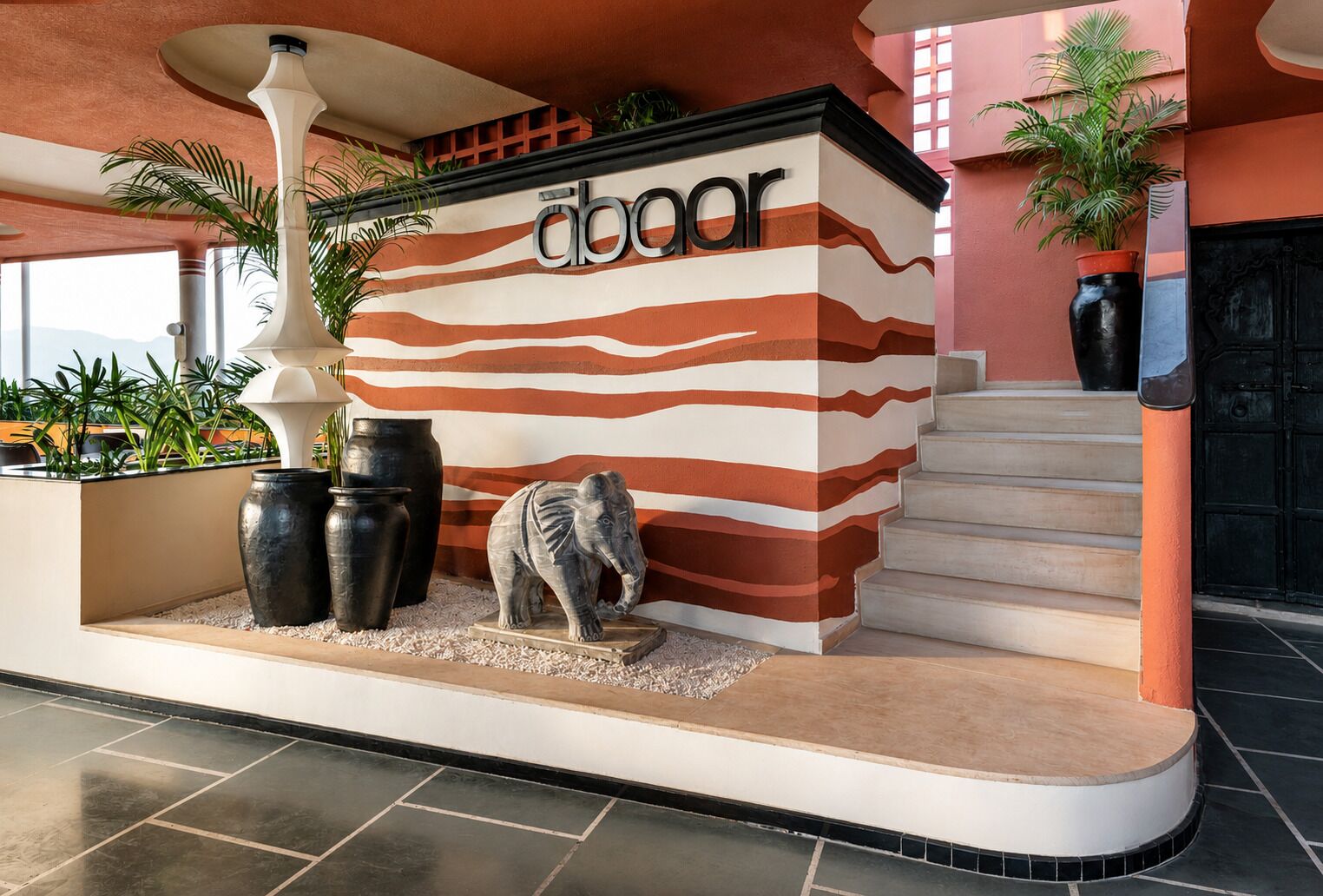 A building entrance with a sign reading 'abcobar,' a staircase, and decorative elements including a sculpture of an elephant and potted plants.
