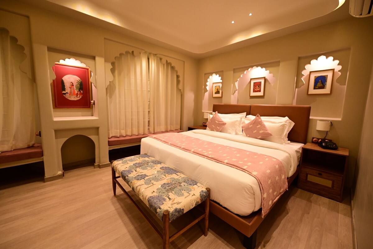 A hotel room with a large bed, a bench, a small seating area, and decorative wall sconces.