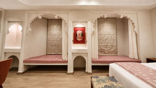 A room with a bed, a bench, and a window with curtains. - My Downtown - The Red Pier (Udaipur)