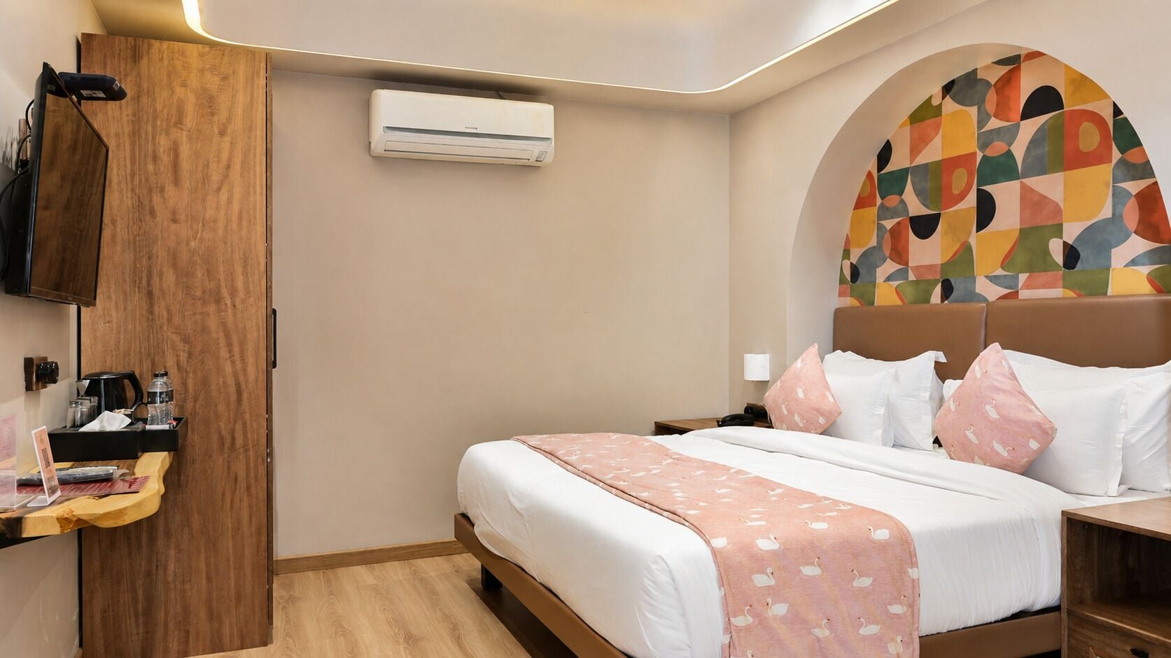 A hotel room with a bed, a bedside table, a wardrobe, and an air conditioning unit.