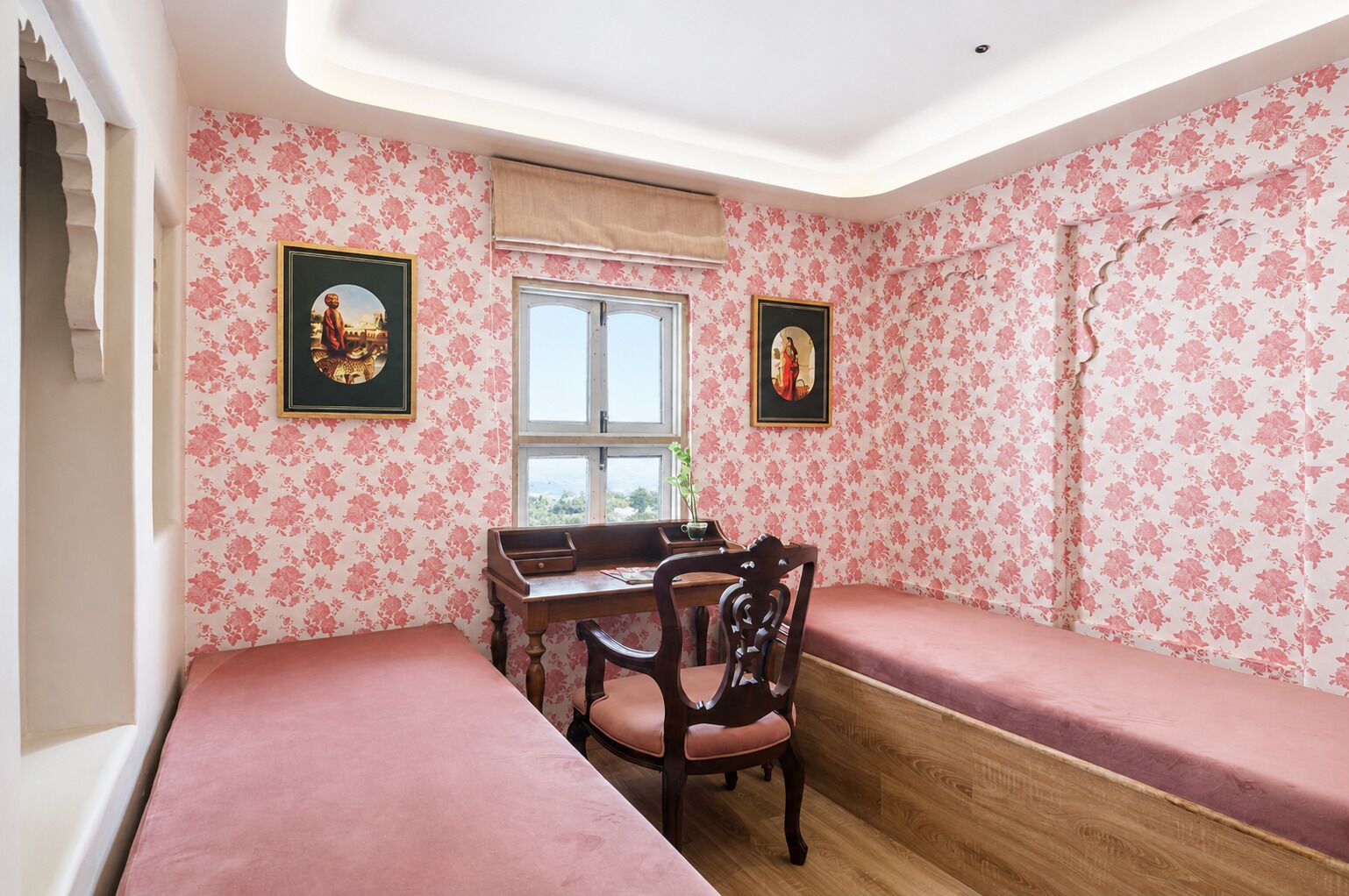 A room with two beds, a desk, and two chairs. There are two framed pictures on the walls.