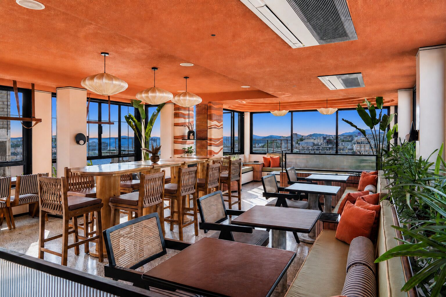 A modern restaurant with a high ceiling, large windows, and a variety of seating options including tables and booths.