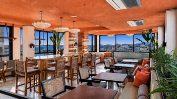 Un restaurante moderno con techo alto, amplios ventanales y diversas opciones de asiento, como mesas y cabinas.