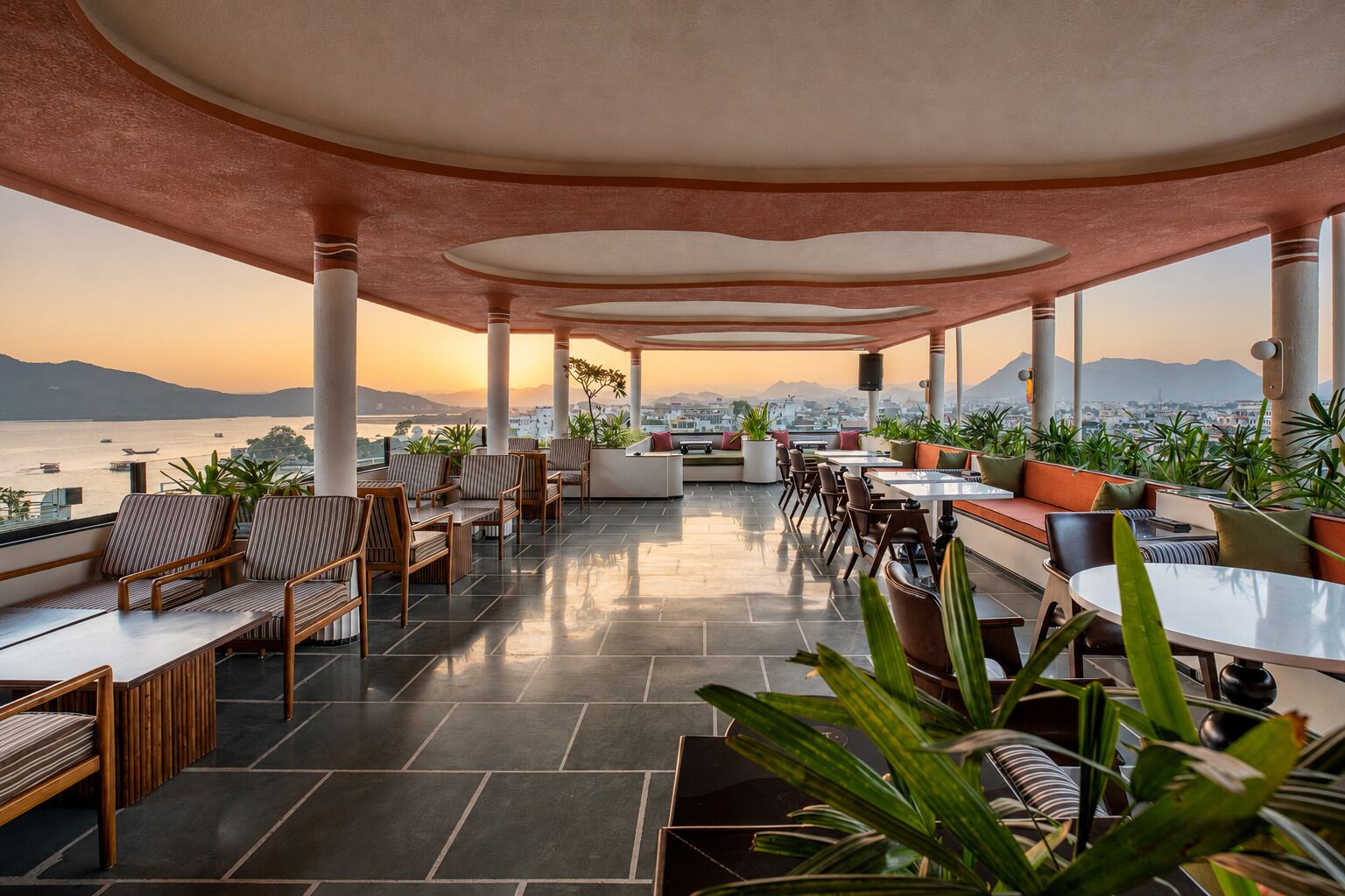 An outdoor seating area with tables and chairs, potted plants, and a view of the city and water.
