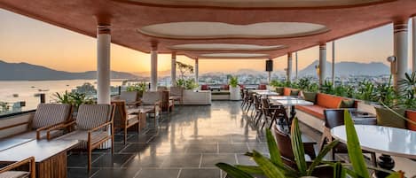 Un espacio al aire libre con mesas y sillas, plantas en macetas y vistas a la ciudad y al agua.