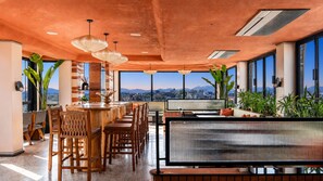 A spacious bar area with wooden furniture and large windows offering a city view.