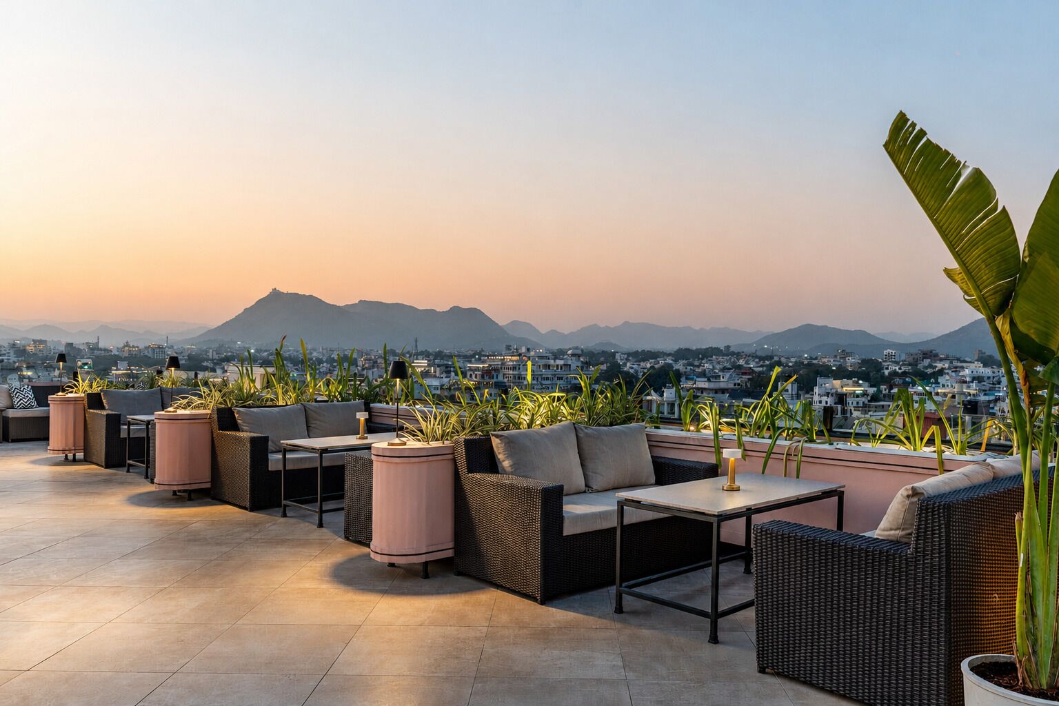 A rooftop terrace with outdoor seating, potted plants, and a cityscape view in the background.