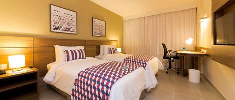 A hotel room with two beds, a desk, a chair, and a large window with curtains.