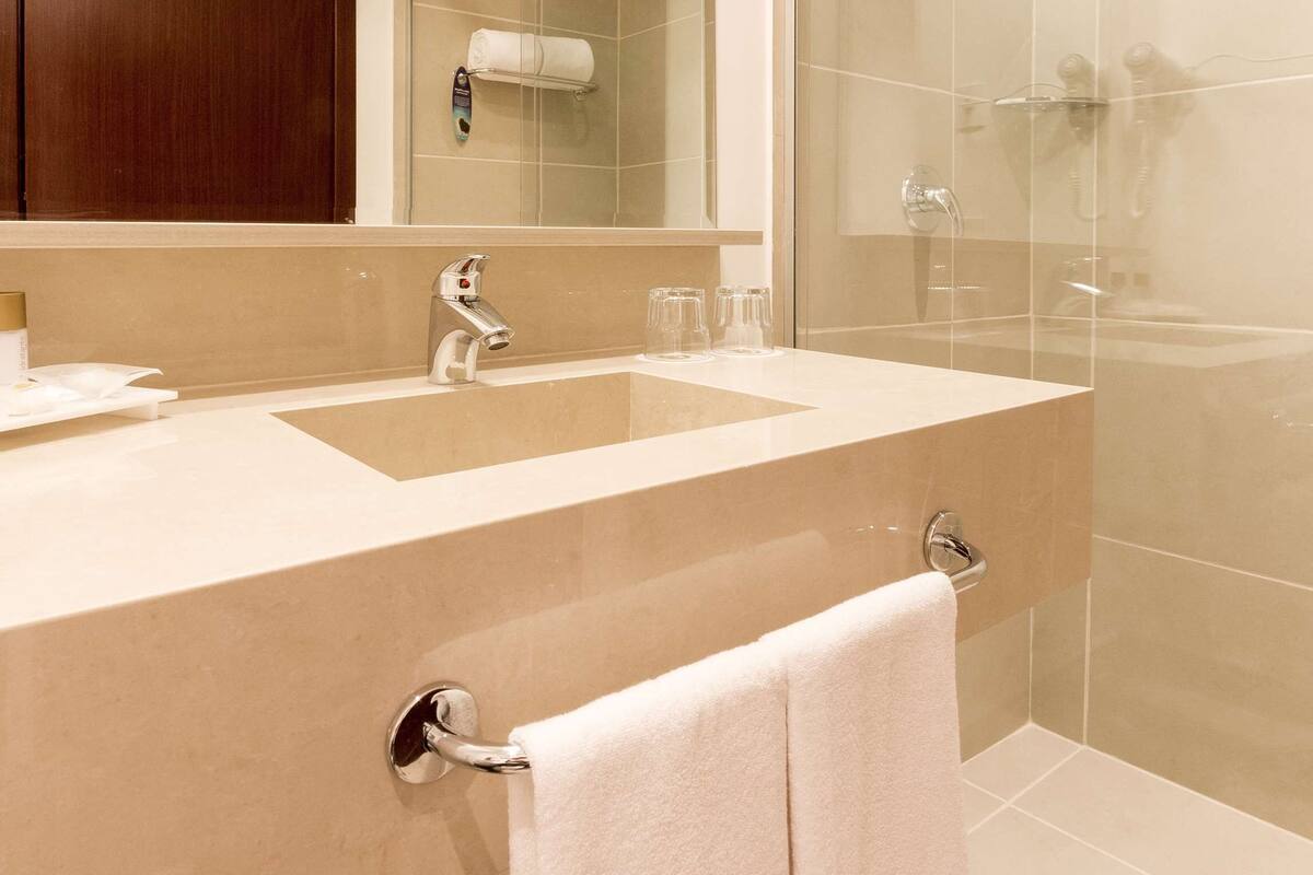 Une salle de bain moderne avec un grand lavabo, un miroir, un porte-serviettes et une cabine de douche en verre.