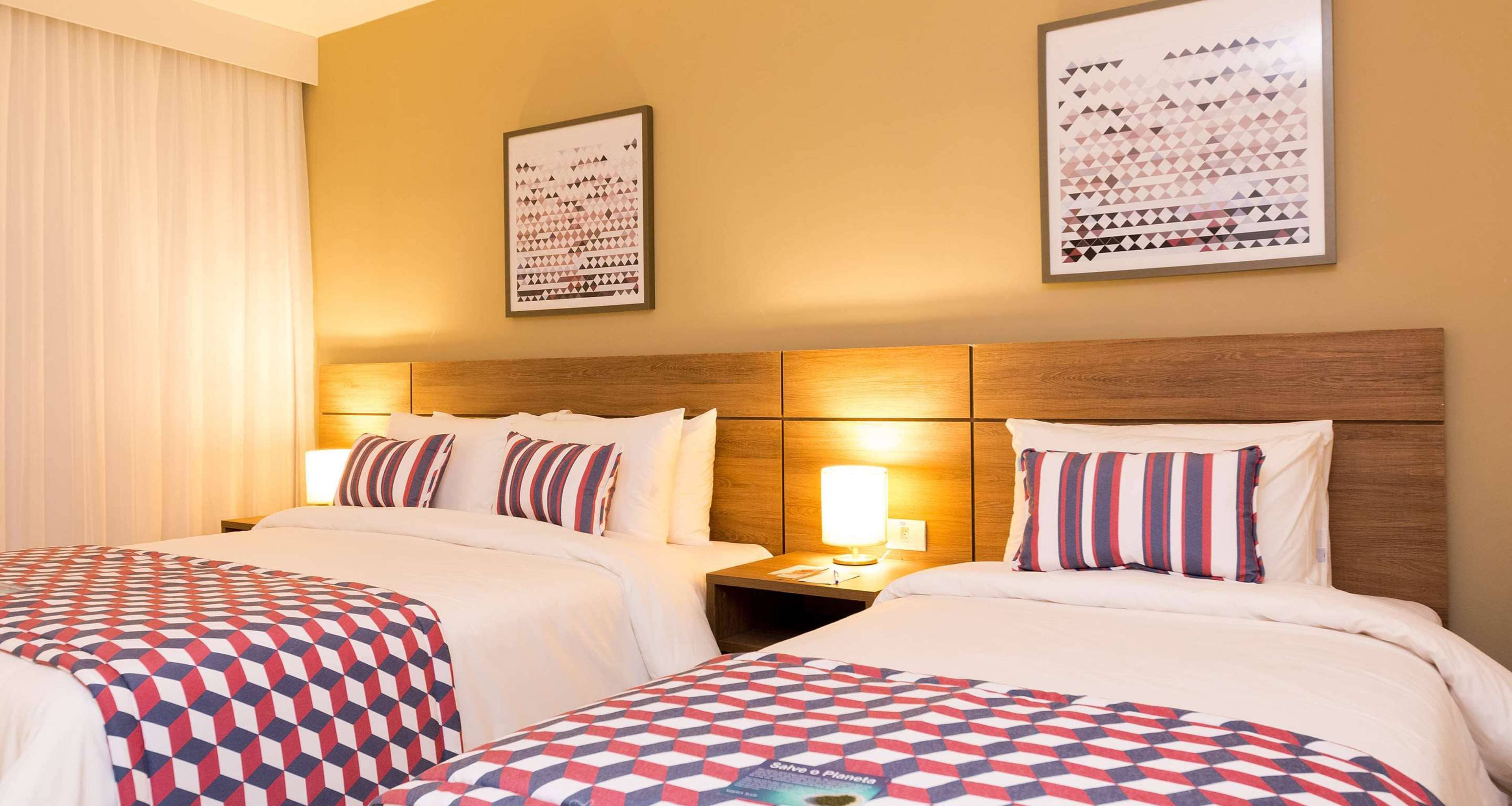 Ein Hotelzimmer mit zwei Betten, jeweils mit einem gemusterten Überwurf, einem hölzernen Kopfteil und einem Nachttisch mit einer Lampe.