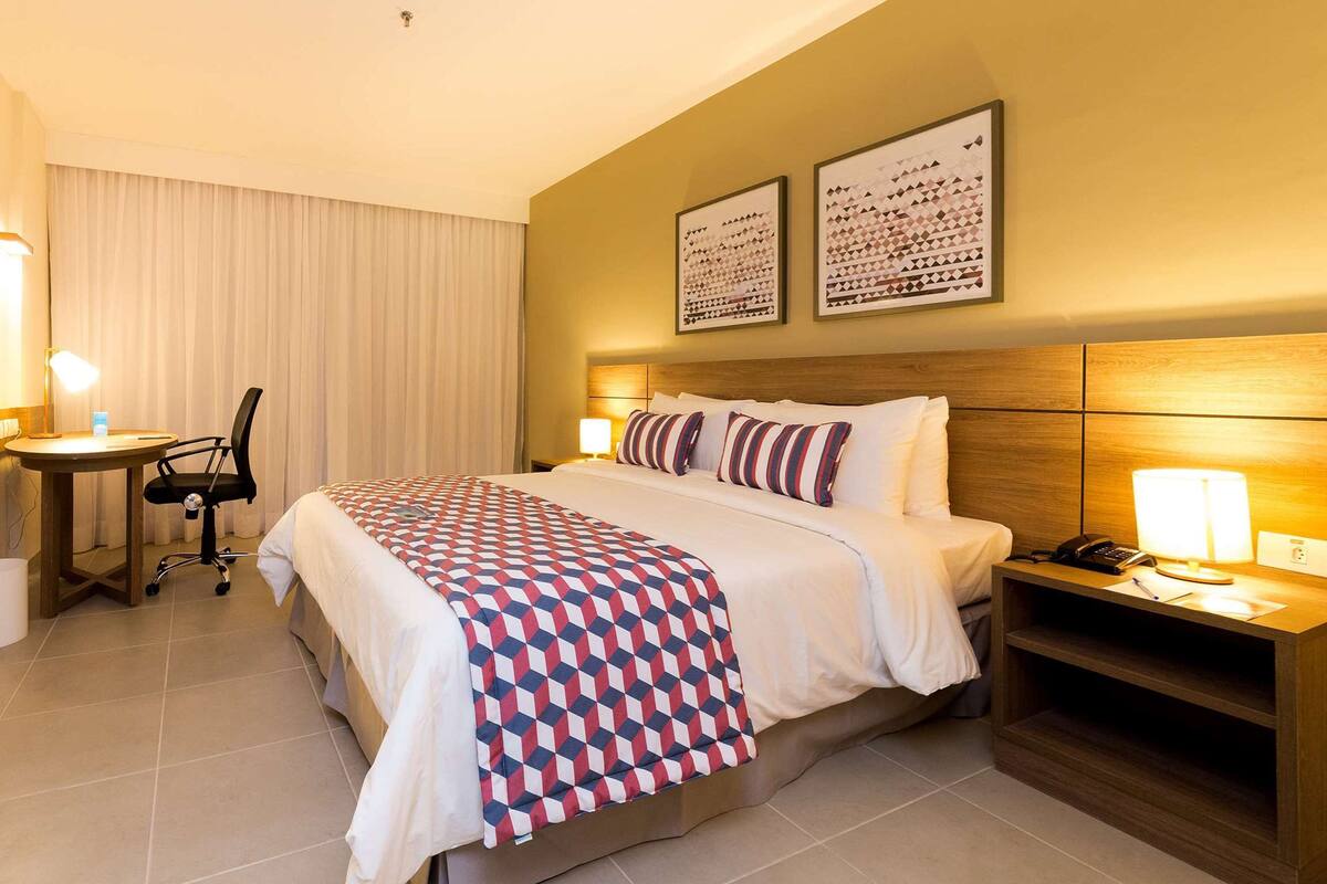 Une chambre d’hôtel avec un lit, un bureau, une chaise, une télévision et deux tableaux encadrés au mur.
