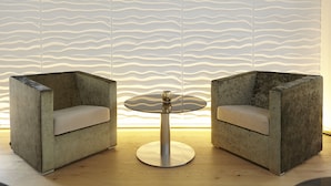 A room with two modern armchairs, a round table, and a textured wall. - Hotel AVA (Neuenkirch)
