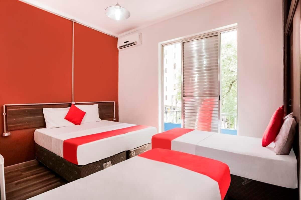 A hotel room with two beds, a window with blinds, and an air conditioning unit.