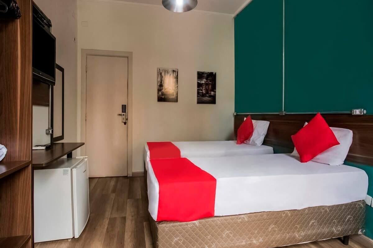 A hotel room with a bed, a small refrigerator, a television, and artwork on the wall.