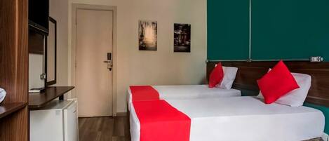 Una camera d'albergo con un letto, un piccolo frigorifero, una televisione e opere d'arte alle pareti.