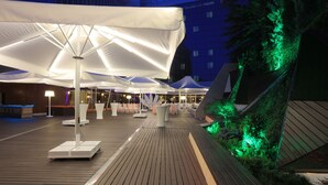 An outdoor deck with white umbrellas, seating areas, and a green-lit vertical garden.