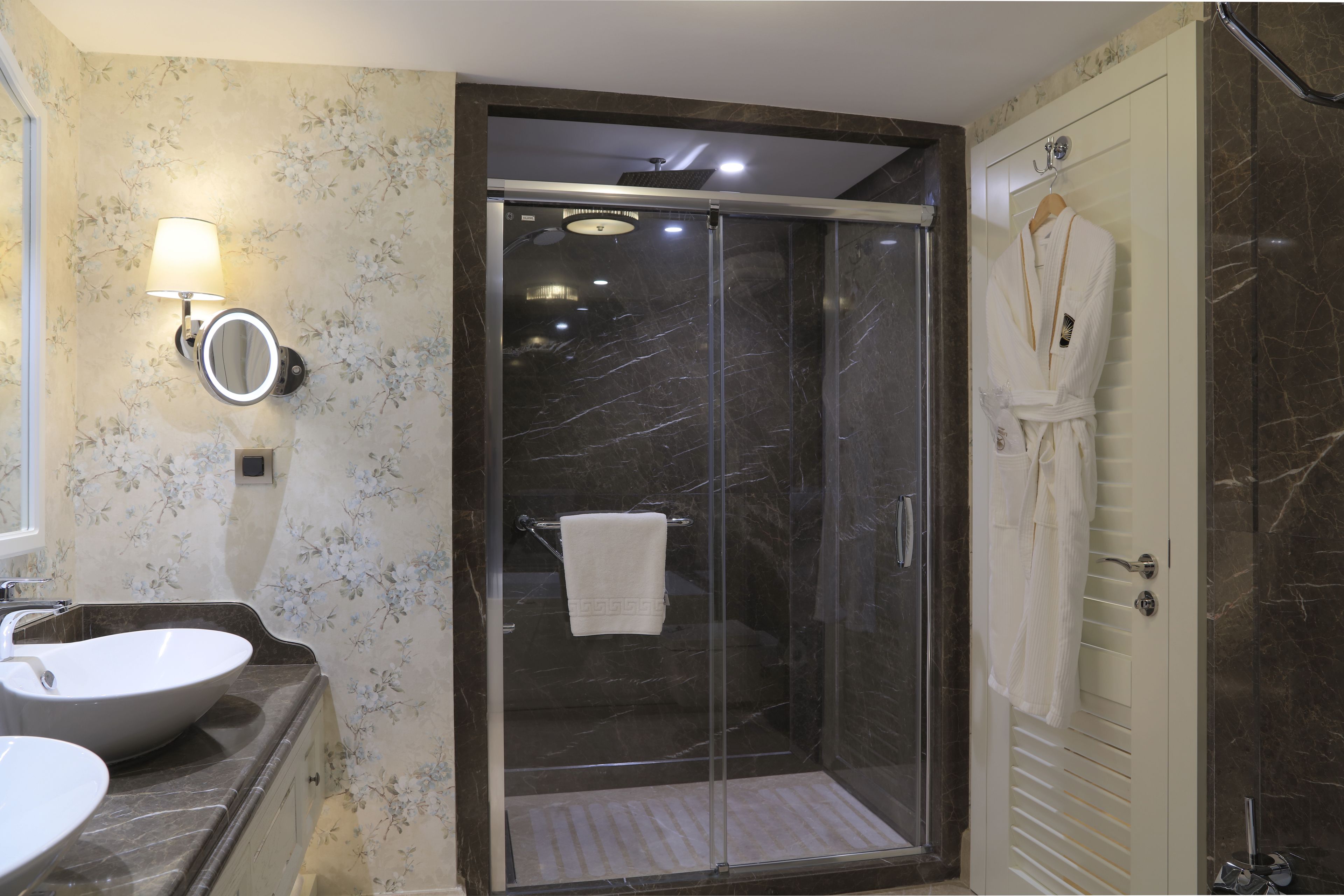 A bathroom with a glass-enclosed shower, a sink, and a robe hanging on the wall.