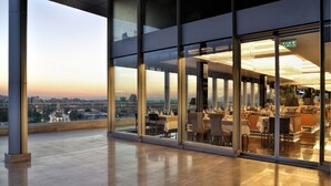 A modern restaurant with a city view, large glass windows, and a polished floor.